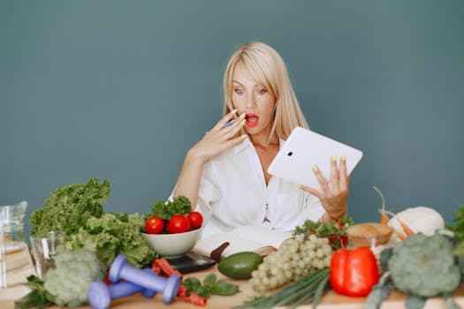 pexels-photo-5622202-5622202 A surprised woman looking at a tablet surrounded by fresh vegetables and fruits, promoting healthy eating.